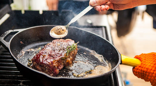 Person cooking steak on a black pan.