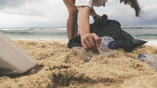 A person picking plastic bottles from the beach.
